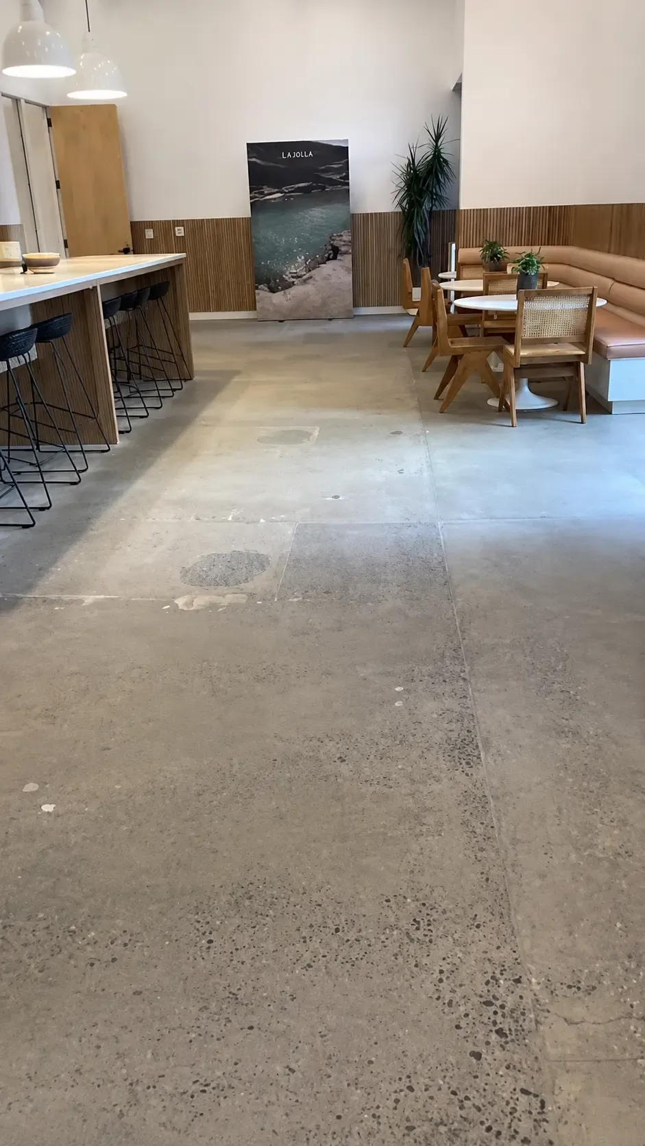 Cafe seating area with a bare concrete floor showing patch repairs and saw-cut joints, before coating.